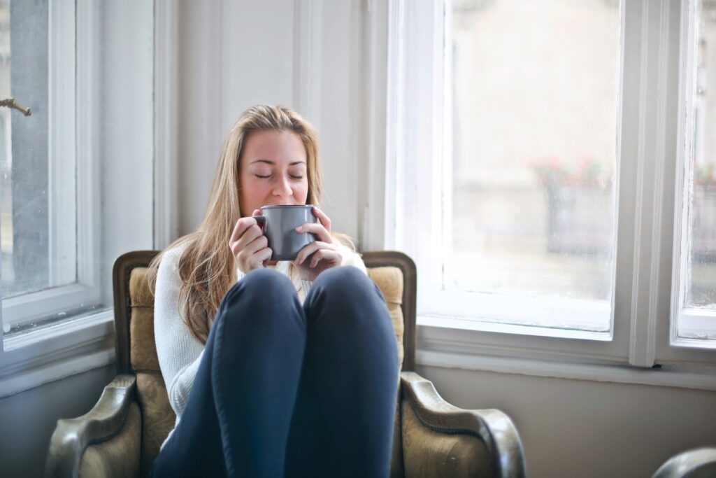 Woman about to sip on mug sitting on a lounge chair with legs on chair