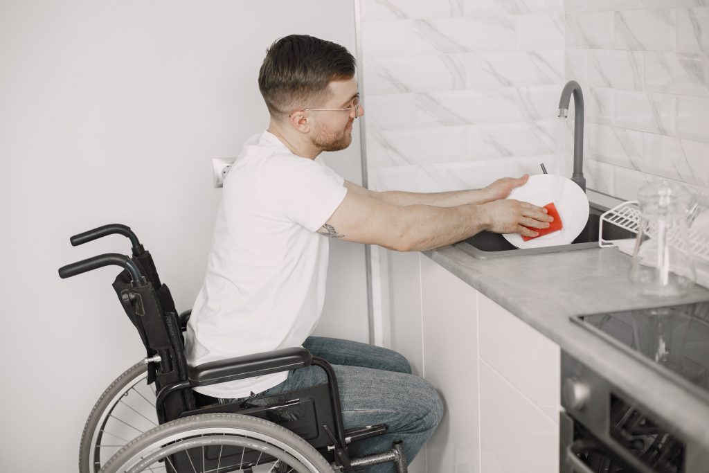 Man in wheelchair Cleaning Dishes In Kitchen
