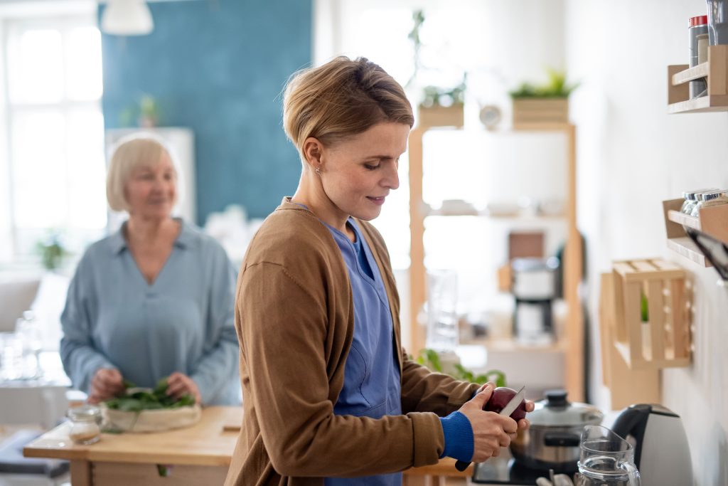 Happy senior woman with support worker indoors, preparing food.