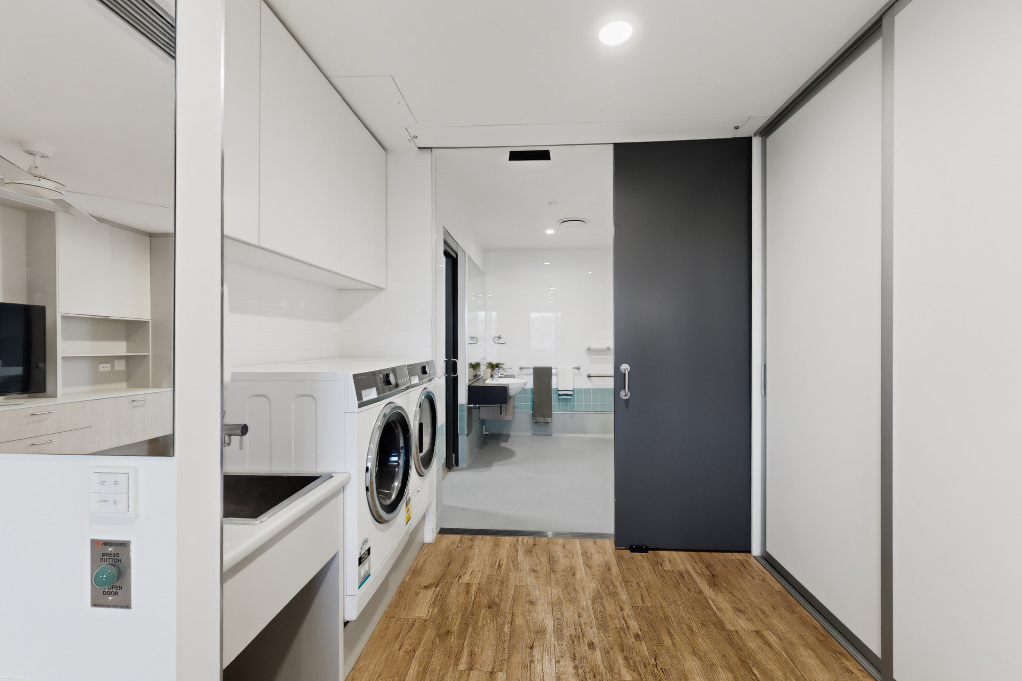 A laundry area with a washing machine next to a sink, with an open doorway leading to a bathroom.