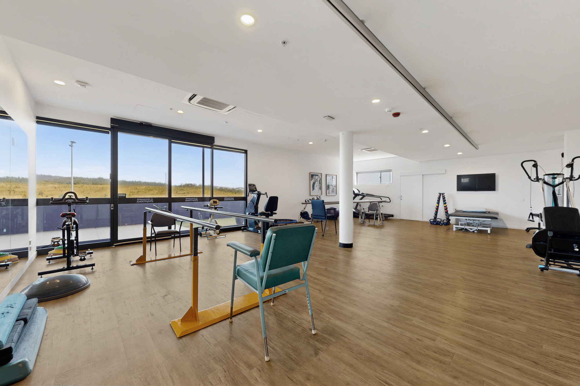 Physical therapy gym featuring parallel bars, exercise chairs, various fitness equipment, and a treatment table.
