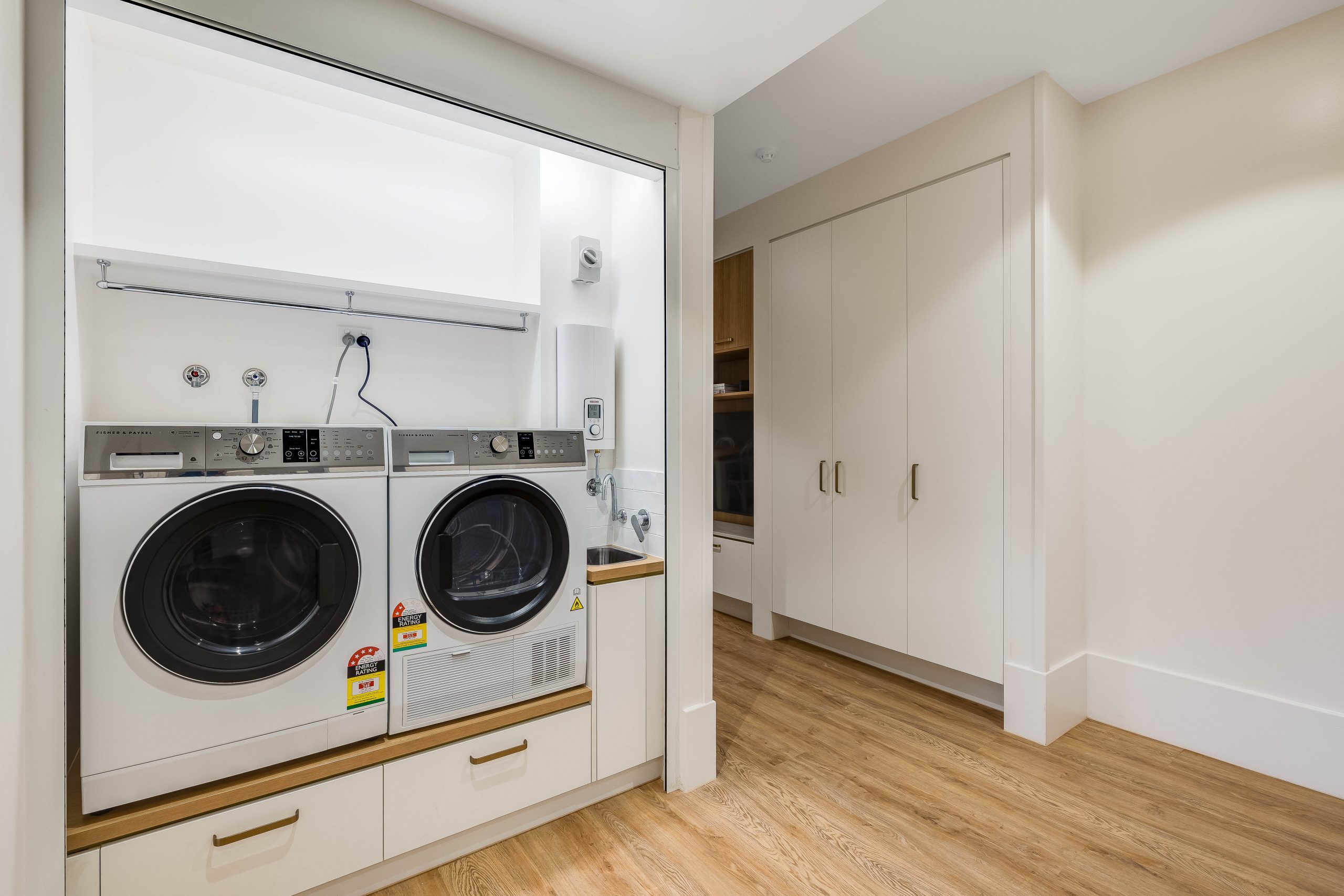 Modern laundry room with a front-loading washer and dryer built into a white alcove, wooden floor, white cabinets, and bright lighting, creating a clean and organized space.