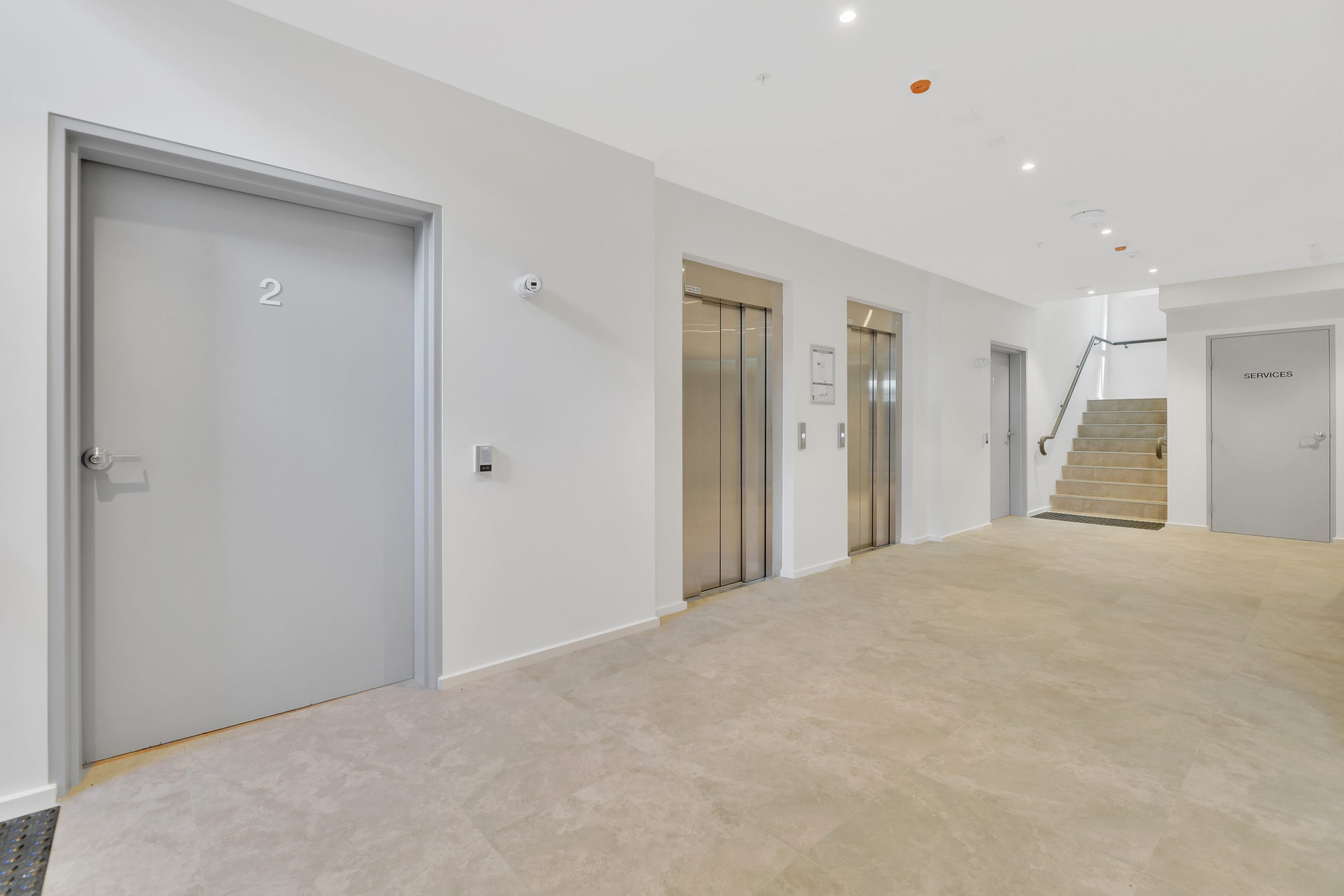 A clean, modern building interior with two closed elevator doors, a door labeled 